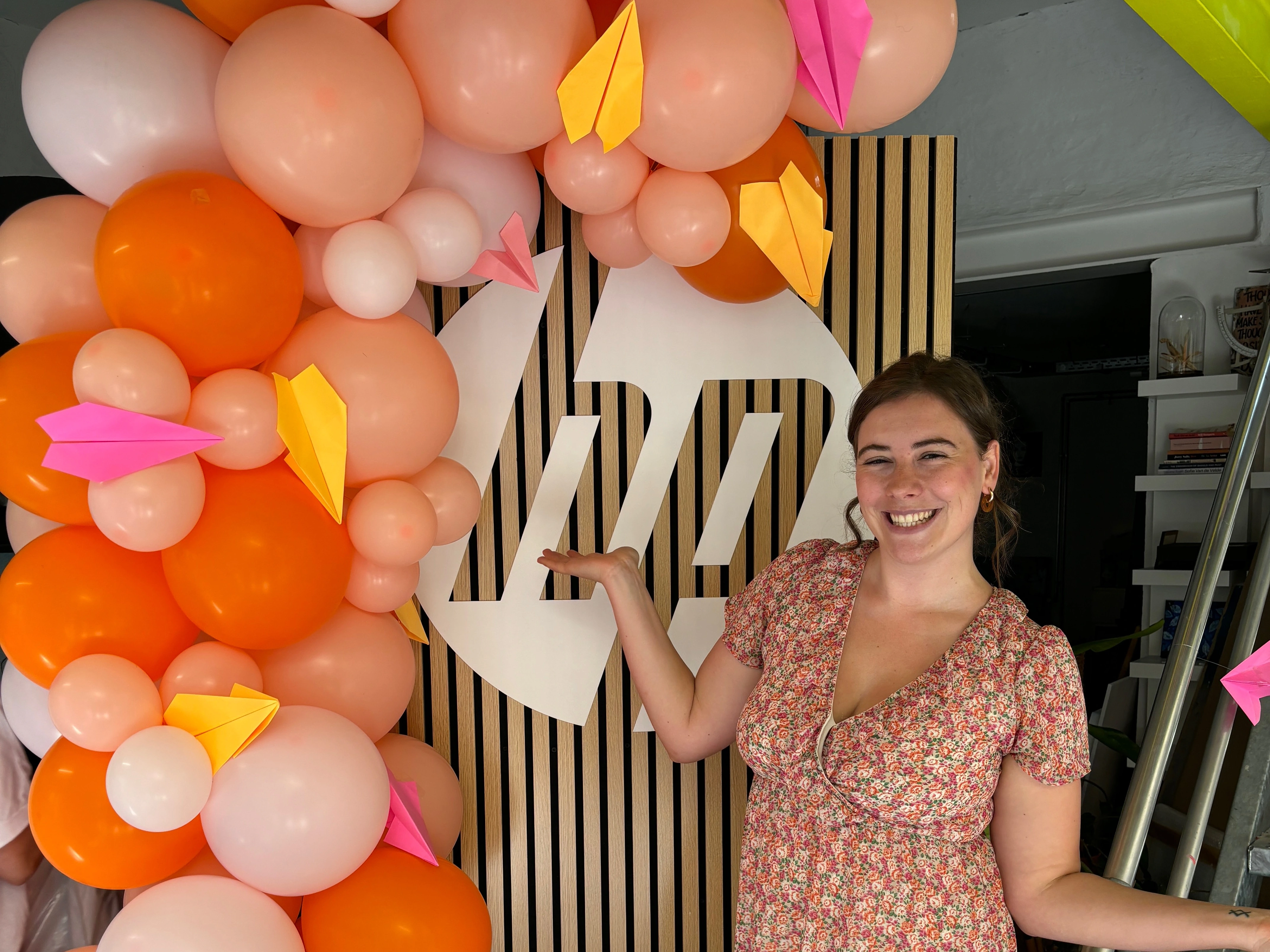 Vrouw poseert naast een kleurrijke ballonnenboog bij een feest.