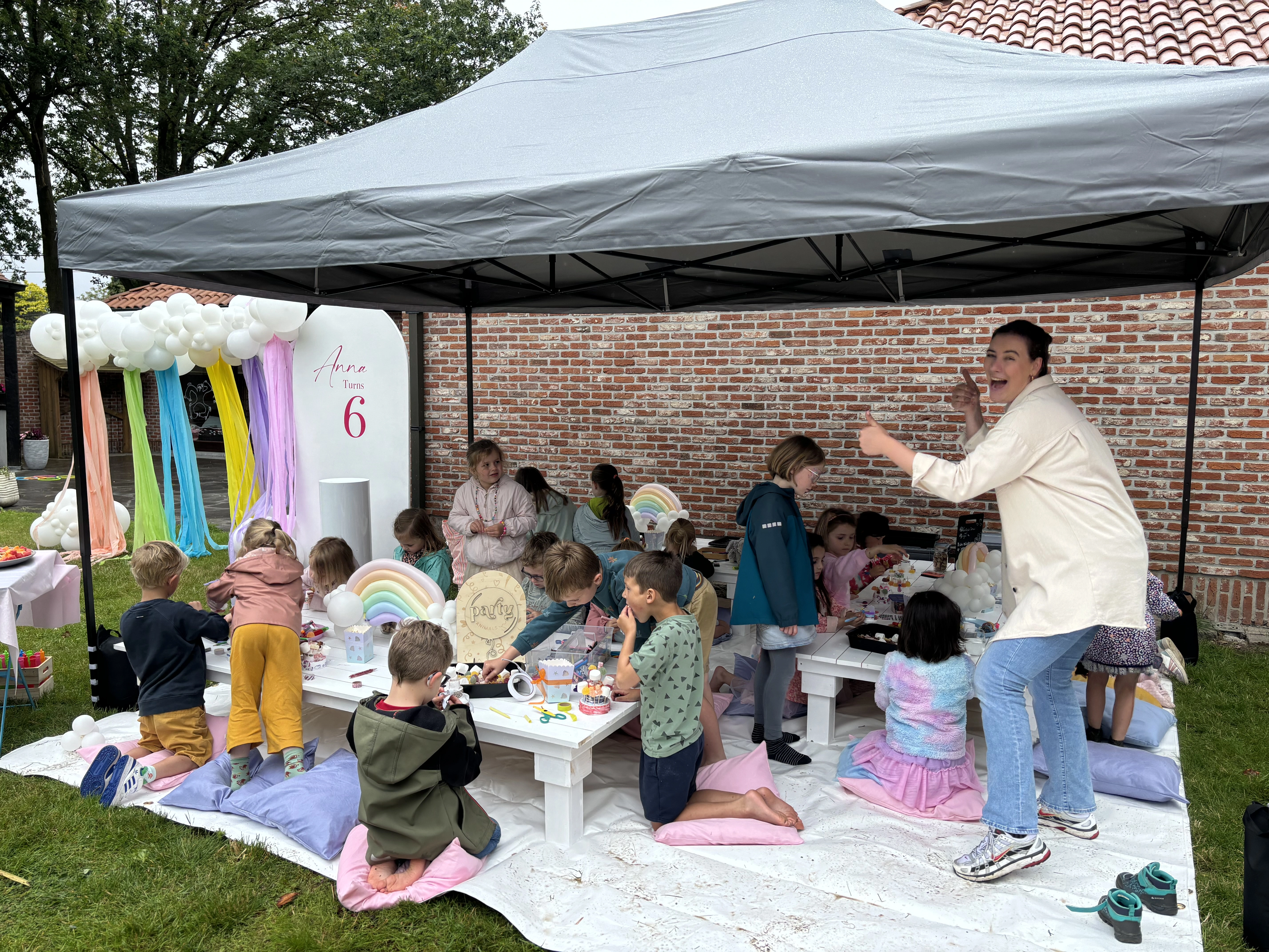 Kinderen knutselen onder een partytent met regenboogdecoratie en ballonnen.