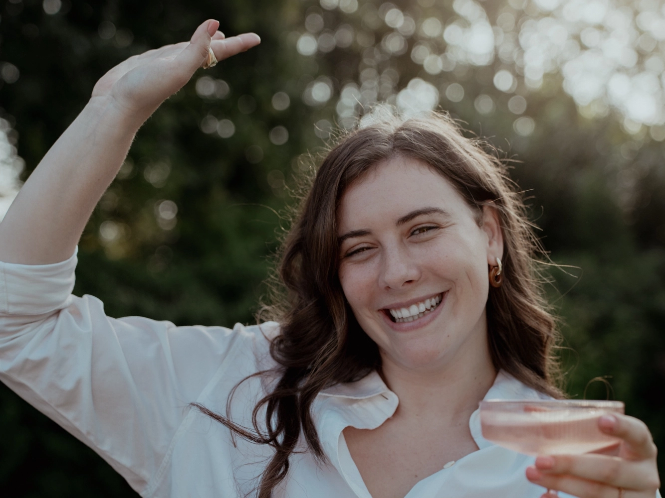 Lachende vrouw met glas roze wijn in een tuin.