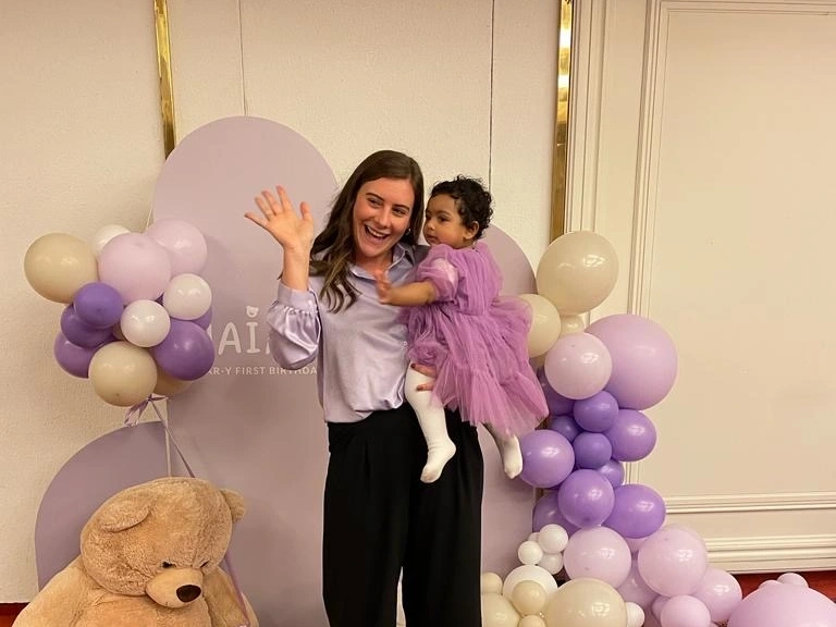 Vrouw met peuter bij paarse ballondecoratie en teddybeer.