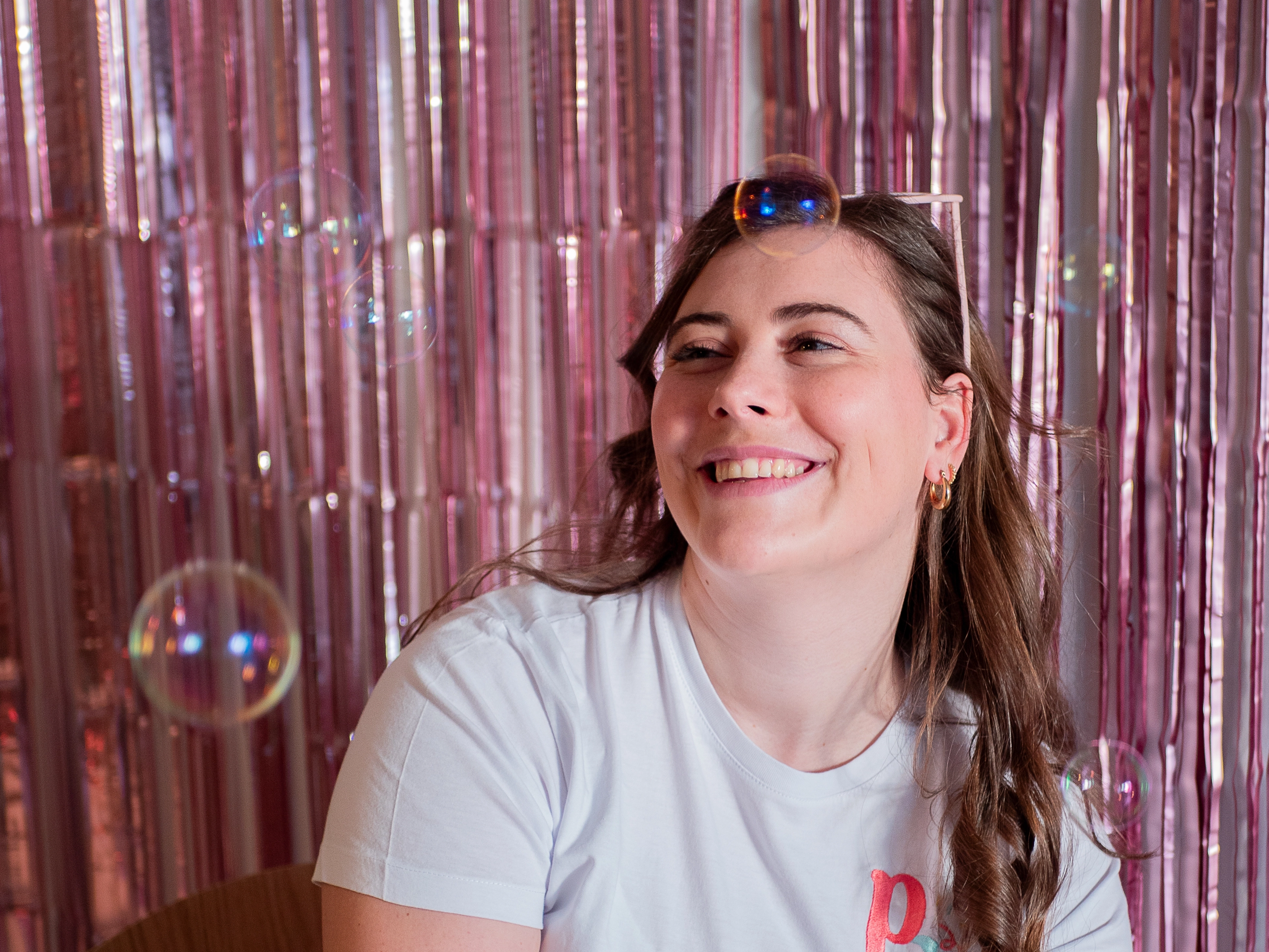 Lachende vrouw voor een roze achtergrond met een zeepbel op haar hoofd.